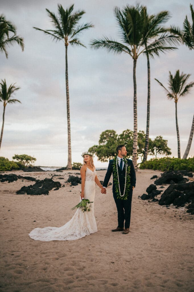 Photograph of couple holding hands under palm trees at Kikaua Point Park In Kailua Kona by Jon Bodhi of Bodhi Weddings